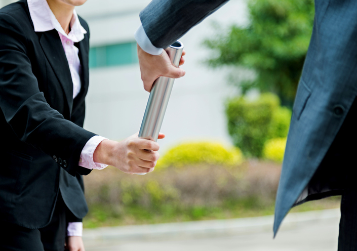 Two professionals run side-by-side, baton at the ready, symbolizing the collaborative and guided approach of effective succession planning.